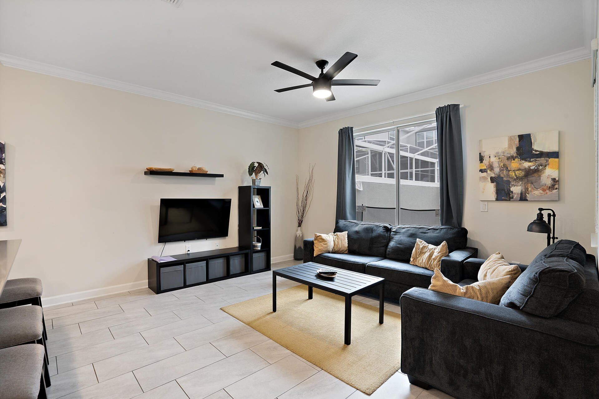 A modern living room with a flat-screen TV, a black sofa, a coffee table, and a ceiling fan.