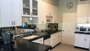 Egy modern konyha fehér szekrényekkel, fekete munkalappal és rozsdamentes acélból készült háztartási gépekkel.