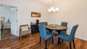 Un comedor con una mesa redonda, cuatro sillas tapizadas en azul, una araña y un letrero decorativo en la pared.