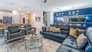 A modern living room with a blue sofa, two armchairs, a coffee table, and a kitchen in the background. - Cgd1249 (Davenport)