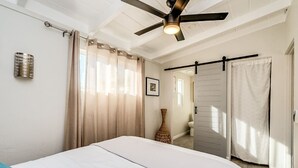 A bedroom with a bed, a ceiling fan, a vase, and a door leading to another room. - Chic Duplex in Tucson 1 of 2 (Tucson)
