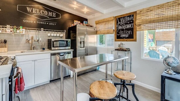 A modern kitchen with stainless steel appliances, a bar area, and a chalkboard with 'Welcome' and 'Good Vibes Only' written on it. - Chic Duplex in Tucson 1 of 2 (Tucson)