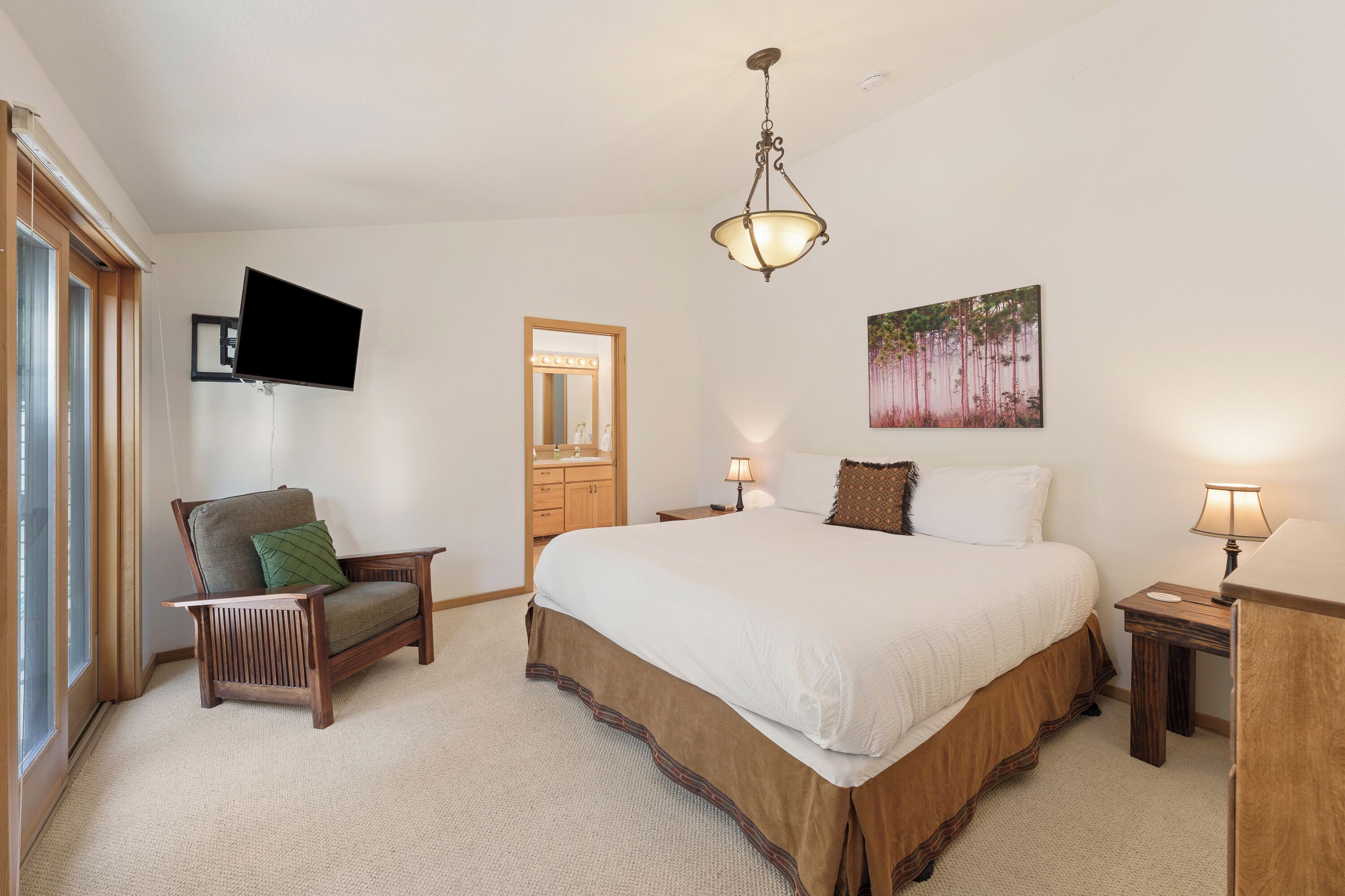 A bedroom with a large bed, a chair, a desk, a mirror, a TV, and a painting on the wall.