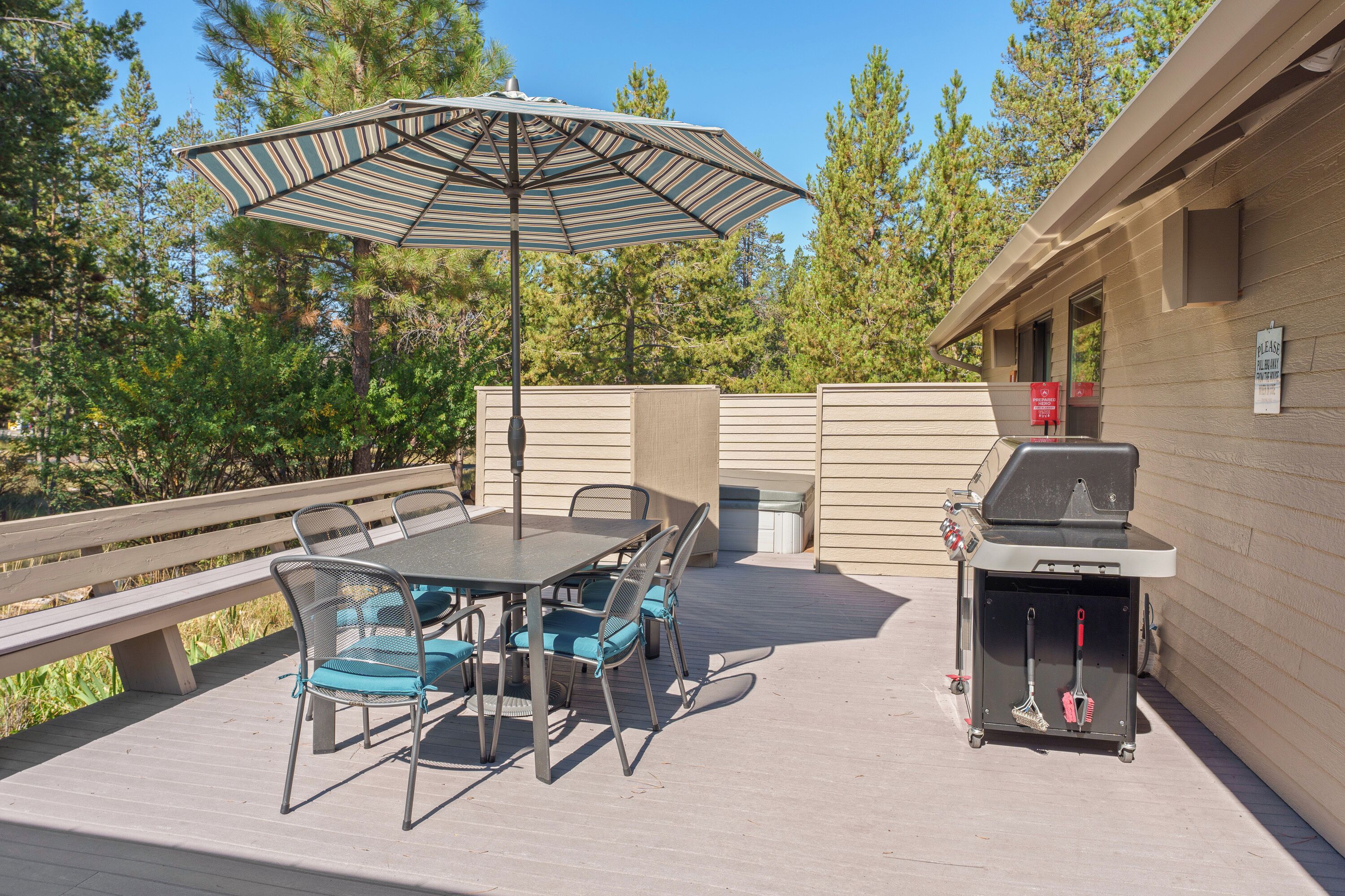 An outdoor patio with a table and chairs, a grill, and a large umbrella.