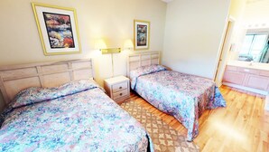 A bedroom with two beds, a nightstand, a lamp, and two framed pictures on the wall. - Club Villas Unit 25A - Lower Level (Sunset Beach)