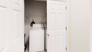 Un espace buanderie équipé d’un lave-linge et d’un sèche-linge à chargement frontal, d’un étendoir métallique et d’une porte donnant sur une autre pièce.