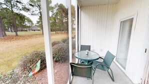 Une véranda avec une table et des chaises en verre, une vue sur une pelouse et une porte avec des stores.