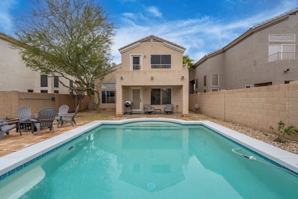 A two-story house with a swimming pool, patio furniture, and a tree.