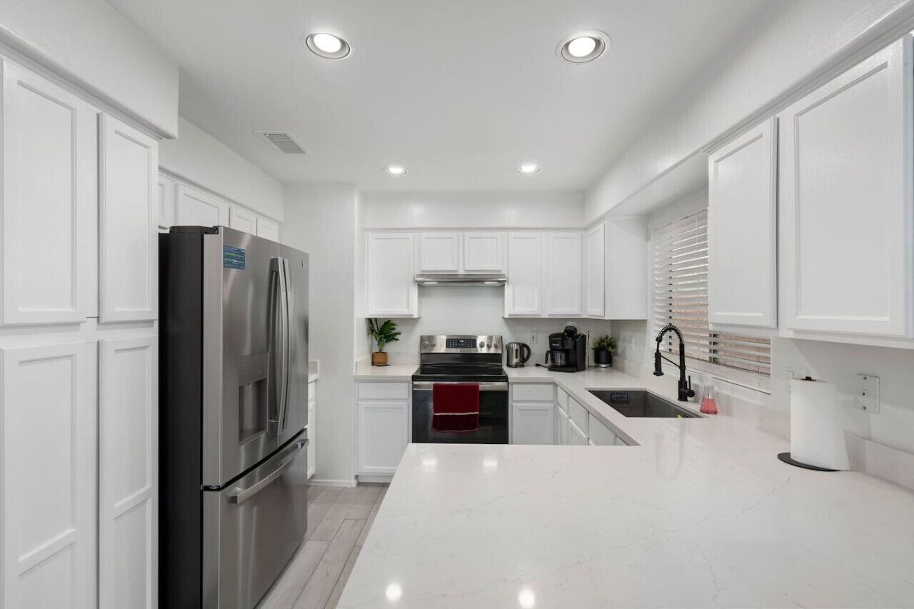 A modern kitchen with white cabinetry, stainless steel appliances, a central island, and recessed ceiling lights.