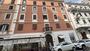 A multi-story building with a row of windows on the ground floor, a white awning with a sign, and a parked car. - Guest House Maison Indipendenza (Rome)