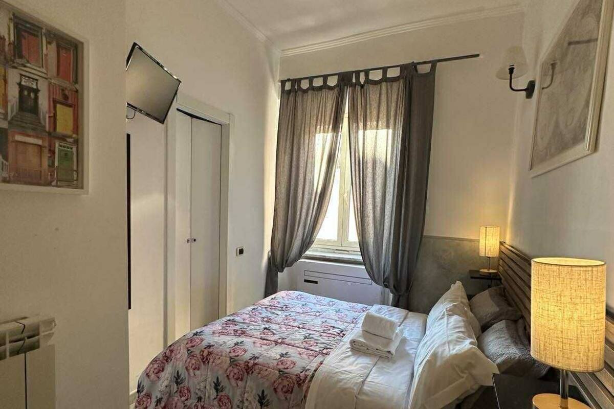 A hotel room with a bed, a bedside lamp, a window with curtains, a radiator, and a wall-mounted picture.