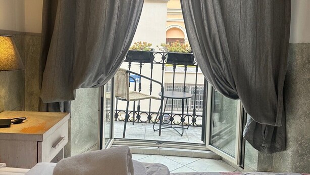 A hotel room with a bed, a bedside table with a lamp, and a view of a balcony with outdoor furniture. - Guest House Maison Indipendenza (Rome)