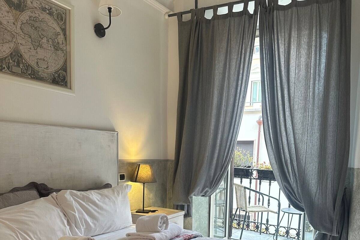 A hotel room with a large bed, a map on the wall, a balcony with a view, and a window with curtains.