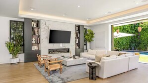 A modern living room with a fireplace, a white sofa, wooden chairs, and a TV mounted on the wall. - Luxurious Villa in The Heart Of Beverly Hills/West Hollywood (Beverly Hills)