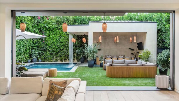 A modern living room with a large glass door leading to a private outdoor area featuring a pool, a wooden deck, and a seating area with a sofa and a coffee table. - Luxurious Villa in The Heart Of Beverly Hills/West Hollywood (Beverly Hills)