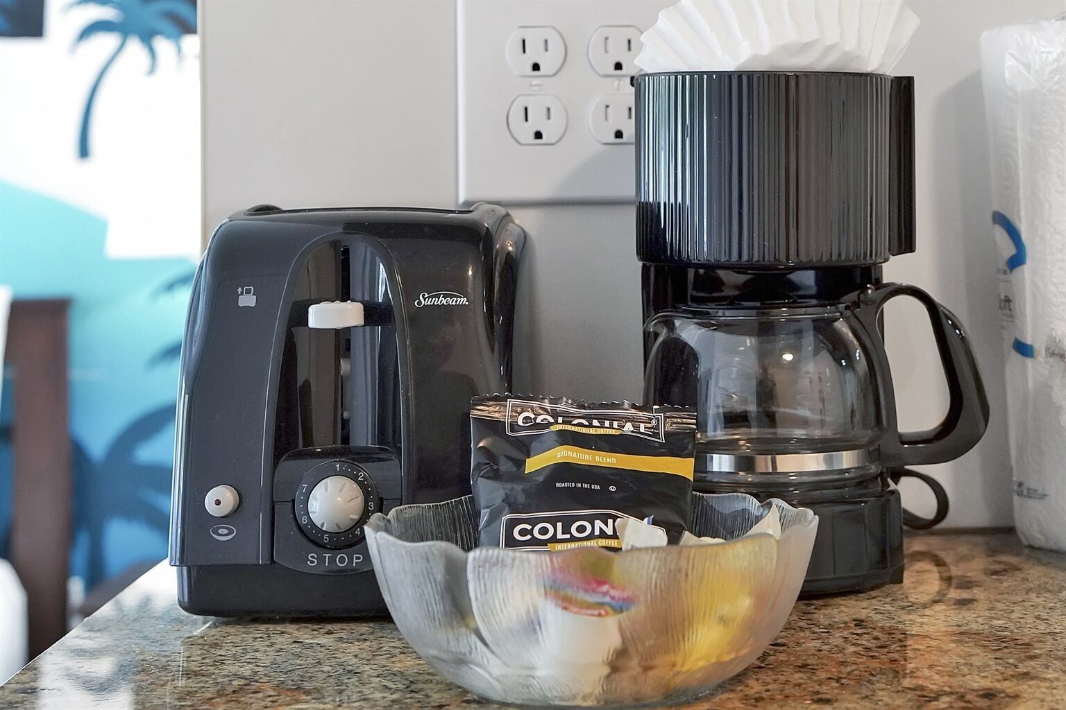 A coffee maker, a bag of coffee, and a bowl on a kitchen counter.