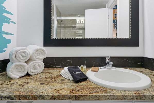 A bathroom with a sink, mirror, towels, toiletries, and a marble countertop. - 6165 Carrier DR #1212 Orlando, 1bed (Orlando)