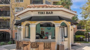 Un bar tiki con un toldo negro, una barra y tres sillas de mimbre.