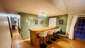 A kitchen with a wooden bar and four stools, a green wall, and a ceiling light fixture. - Secluded Finger Lakes 3BR Retreat Near Keuka Lake with Vineyard Views (Branchport)