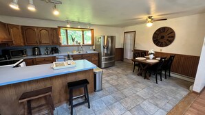 A kitchen with a central island, bar stools, a dining table with chairs, a refrigerator, a microwave, and a clock on the wall. - Secluded Finger Lakes 3BR Retreat Near Keuka Lake with Vineyard Views (Branchport)