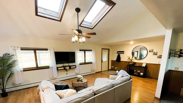 A spacious living area with a large sofa, a ceiling fan, skylights, a flat-screen TV, and a wooden floor. - Secluded Finger Lakes 3BR Retreat Near Keuka Lake with Vineyard Views (Branchport)