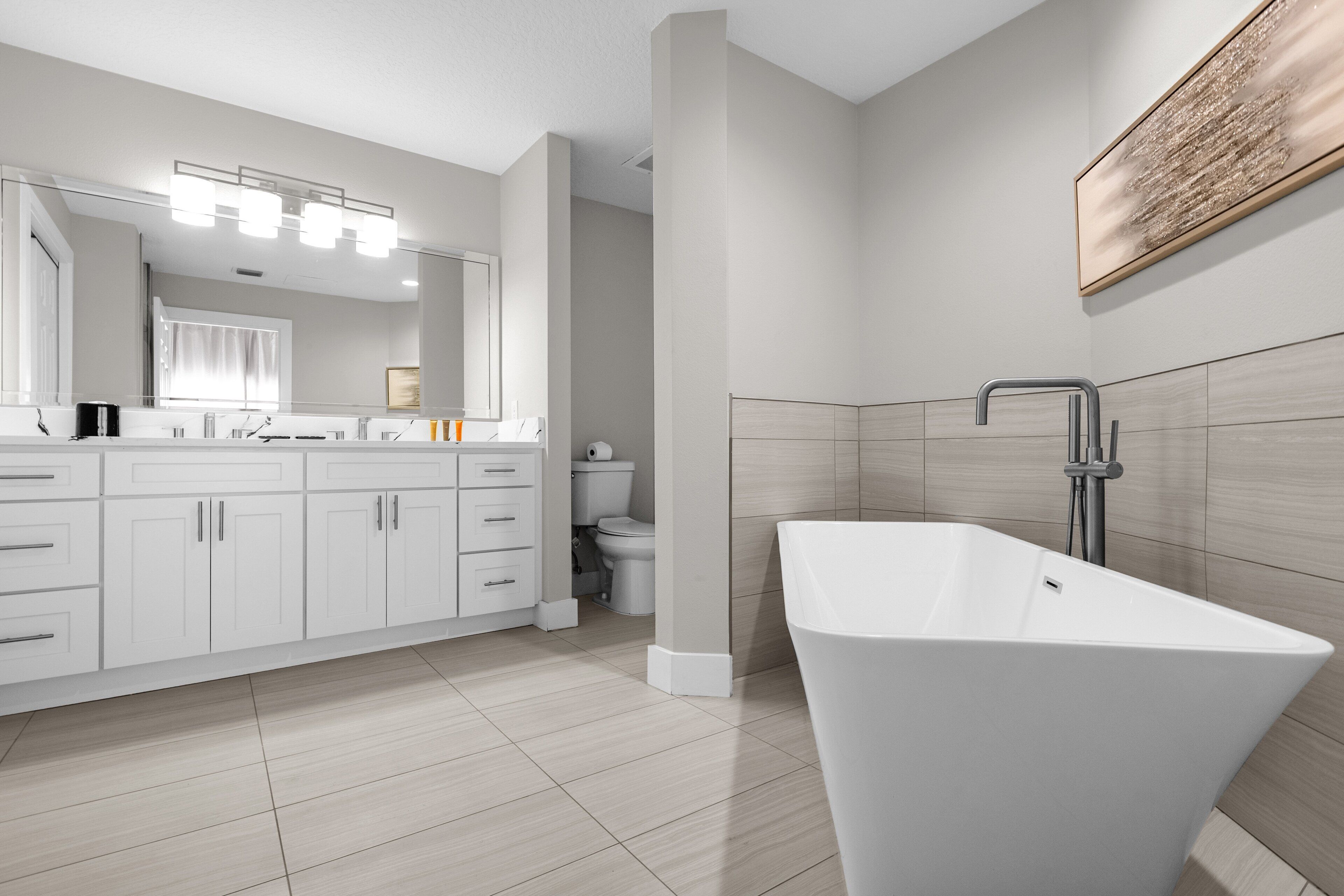 A modern bathroom with a freestanding bathtub, white cabinetry, and a large mirror.