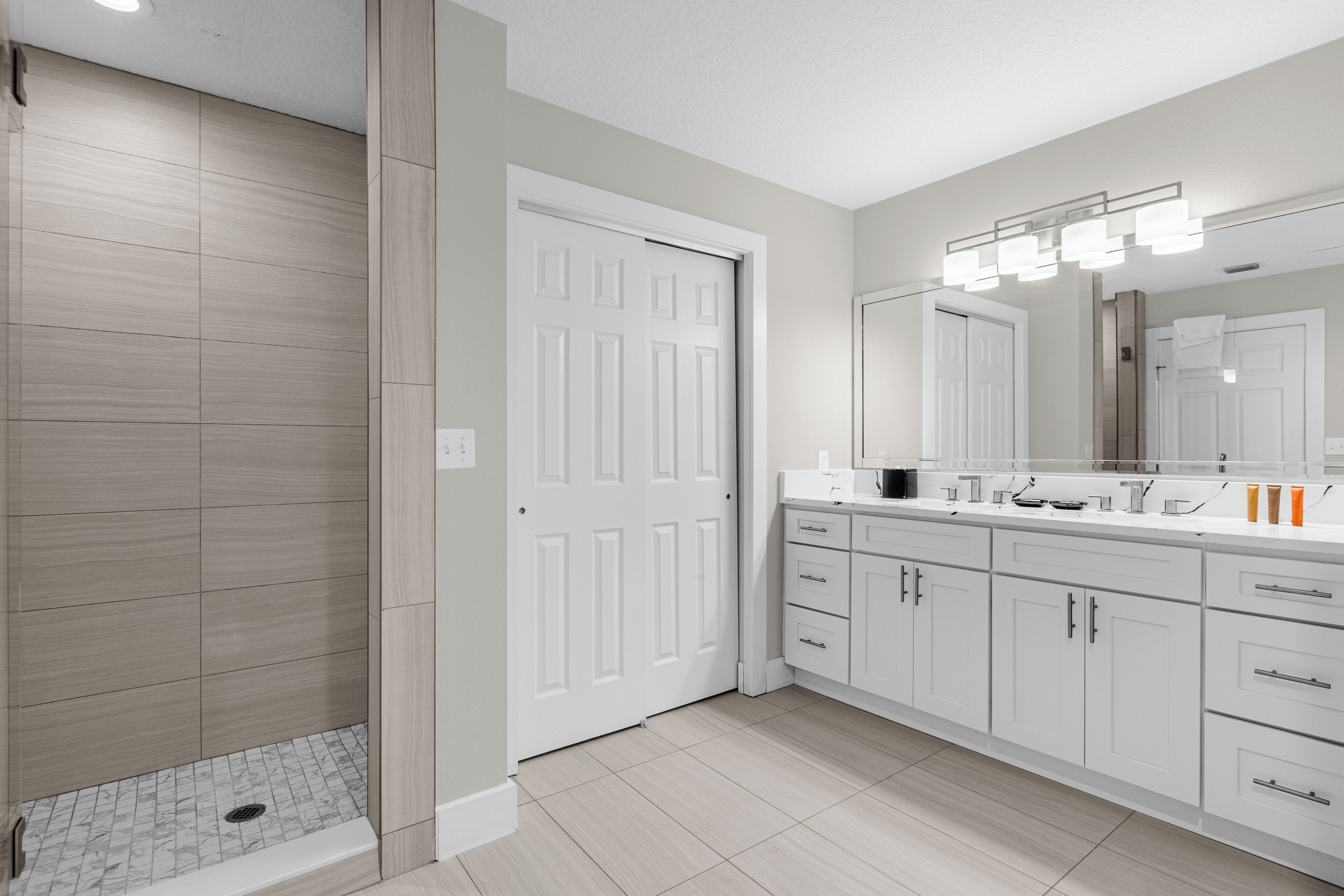 A modern bathroom with a walk-in shower, a large mirror, and a vanity with a sink and cabinet.