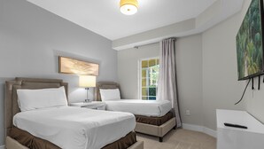 Ein Hotelzimmer mit zwei Betten, einem Schreibtisch, einer Lampe, einem Gemälde und einem Fenster mit Vorhängen.
