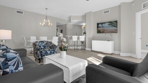 Ein modernes Wohnzimmer mit Deckenventilator, einer Chandelierleuchte und einem Essbereich mit weißen Möbeln.