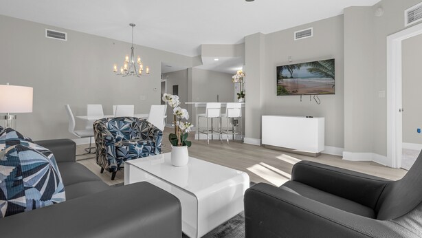 Un soggiorno moderno con una ventola a soffitto, un lampadario e un'area pranzo con mobili bianchi.