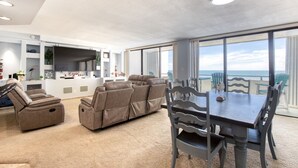 Uma sala de estar espaçosa com uma grande janela com vista para o mar, uma mesa de jantar com cadeiras e um conjunto de sofás.