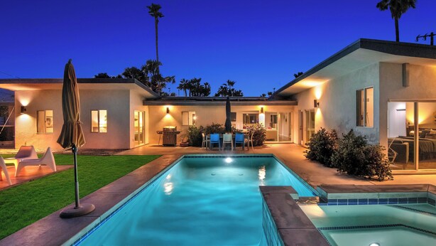 Une piscine avec un espace patio, un coin salon couvert et un bâtiment bien éclairé au design moderne.
