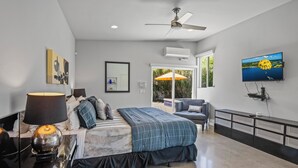 Une chambre moderne avec un lit, un ventilateur de plafond, une télévision et une vue sur l’extérieur.