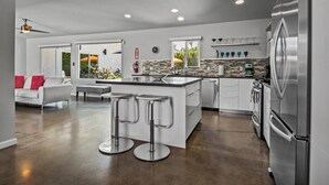 Une cuisine moderne dotée d’un îlot central, d’appareils électroménagers en acier inoxydable et d’un coin bar avec des tabourets.