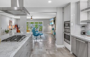A modern kitchen with a central island, stainless steel appliances, and a seating area with blue chairs. - Farrell 2 (Palm Springs)