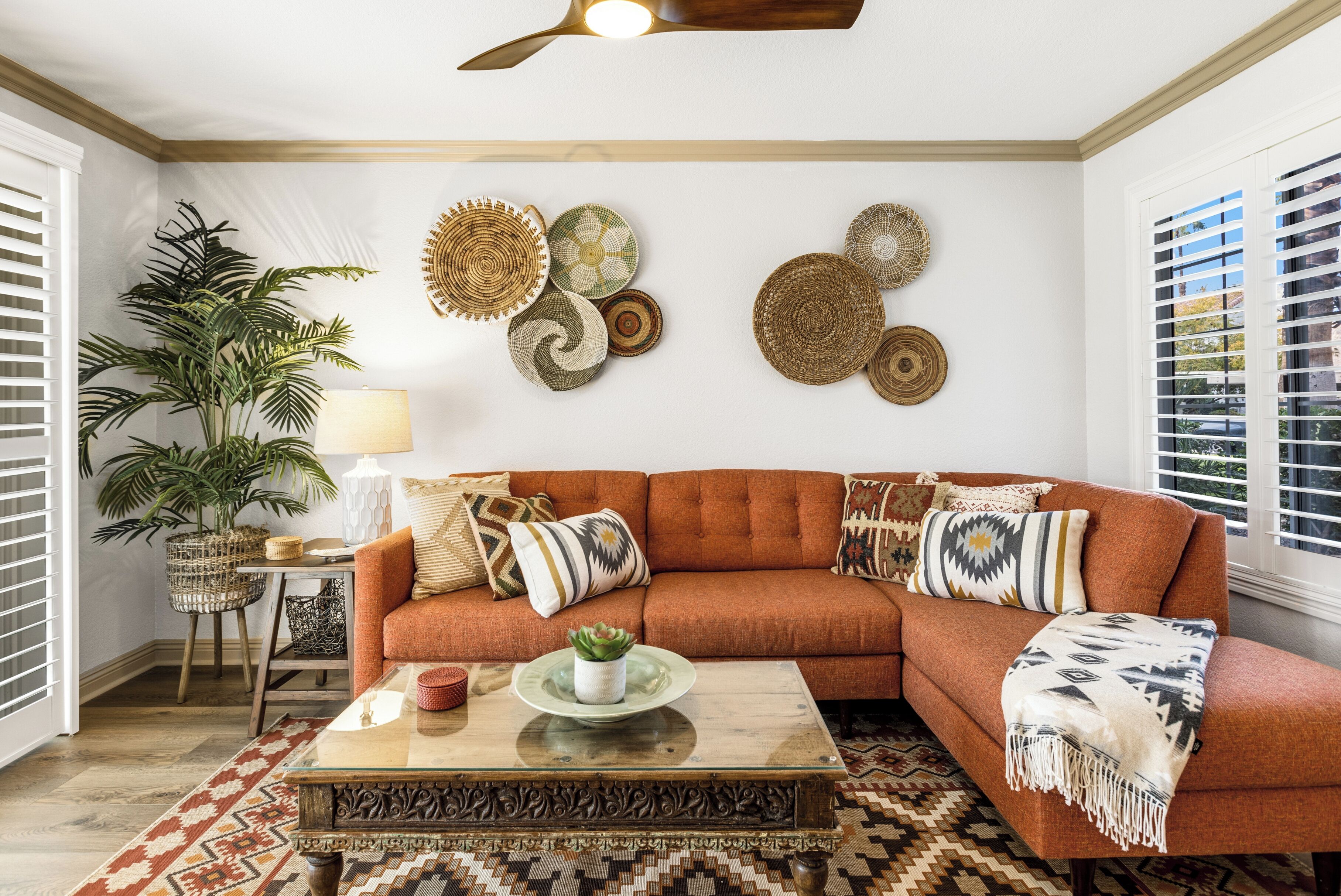 A living room with a sectional sofa, decorative wall hangings, a potted plant, and a patterned rug.