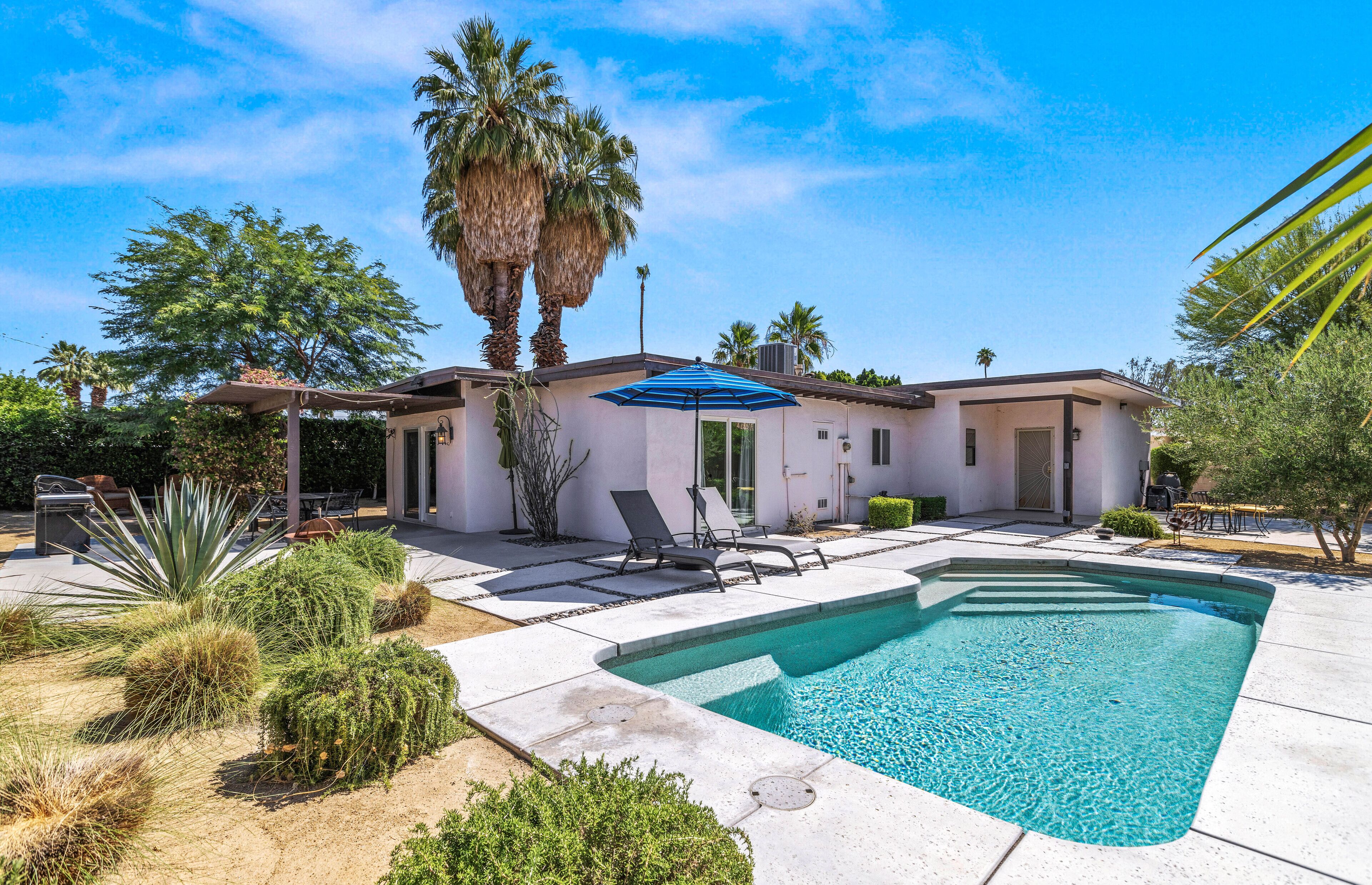 A modern house with a swimming pool, patio furniture, and palm trees.