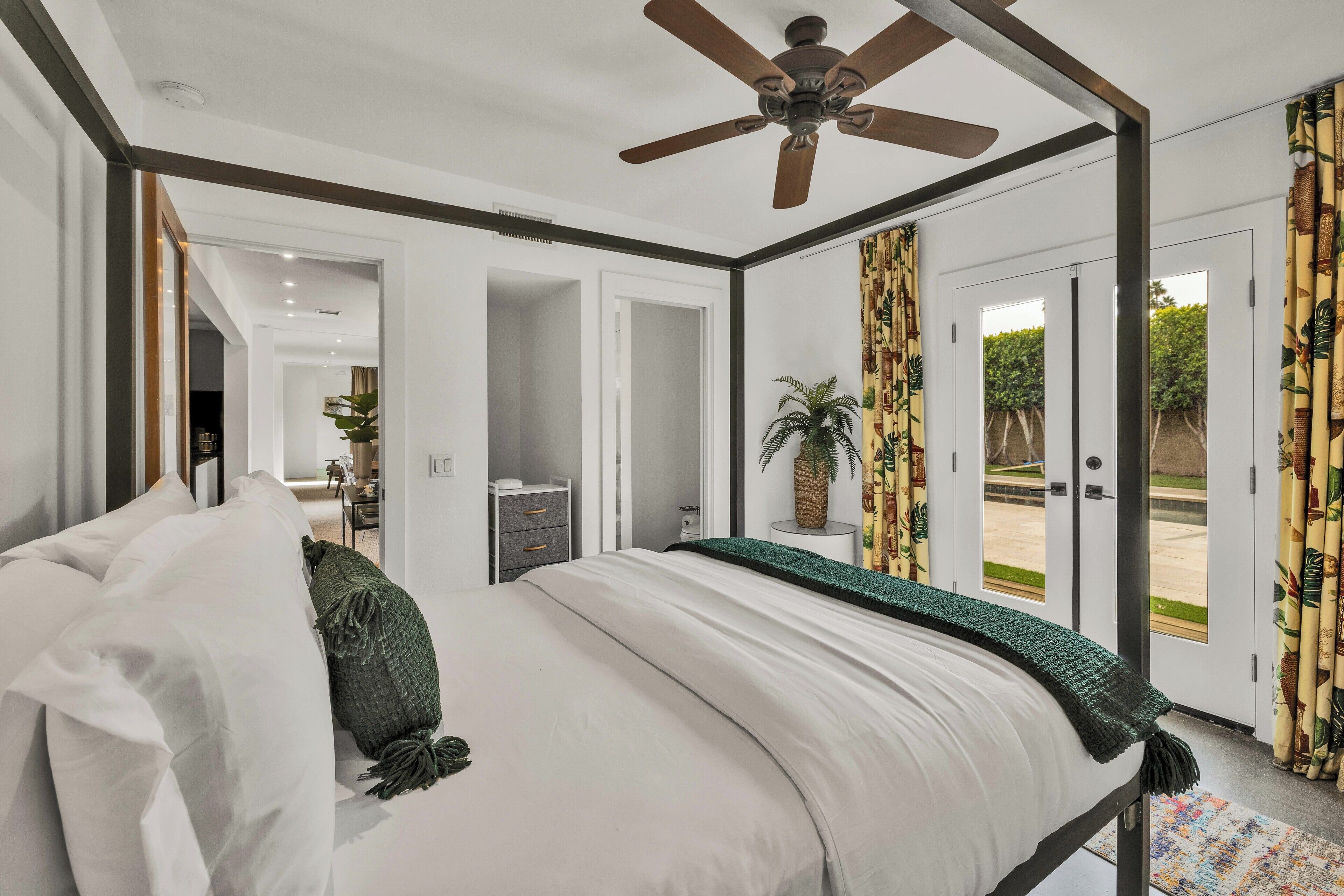 A bedroom with a four-poster bed, a ceiling fan, and a view of the outdoors through a door.