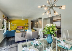 A modern living room with a sofa, dining table, and chairs. There is a kitchen area in the background. - Via Escuela 3 (Palm Springs)