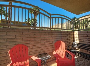 Un patio con dos sillas Adirondack rojas, una mesita y un banco.