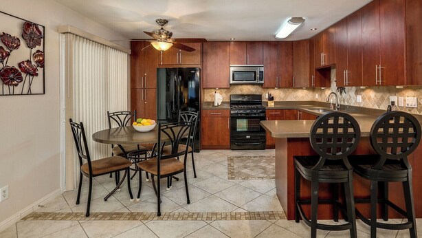 Une cuisine moderne avec des meubles en bois, un réfrigérateur noir, un four à micro-ondes et une cuisinière. On y trouve une table à manger avec des chaises et un ventilateur de plafond.