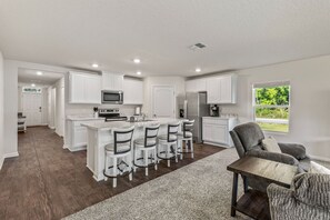 A modern kitchen with white cabinetry, a central island with bar stools, and a refrigerator. - Swaying Palm Cabana by the Beach (Palm Coast)