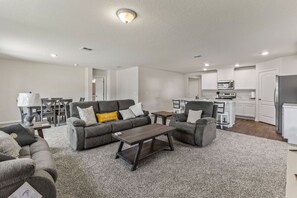 A modern living room with a grey sofa set, a coffee table, and a dining area with a table and chairs. - Swaying Palm Cabana by the Beach (Palm Coast)