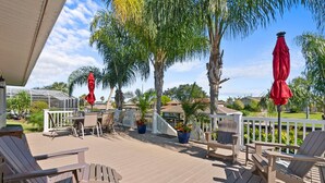 A wooden deck with outdoor furniture, including chairs and a table, surrounded by palm trees and potted plants. - Dockside Serenity (Palm Coast)
