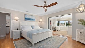 A bedroom with a bed, nightstands, a ceiling fan, a large window, and a view of the outdoors. - Dockside Serenity (Palm Coast)
