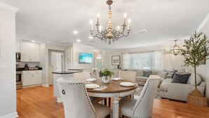 A modern kitchen with white cabinets, a dining table set for four, and a chandelier. - Dockside Serenity (Palm Coast)