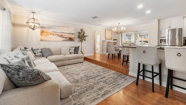 A modern living room with a sectional sofa, a dining area, and a kitchen with bar stools. - Dockside Serenity (Palm Coast)