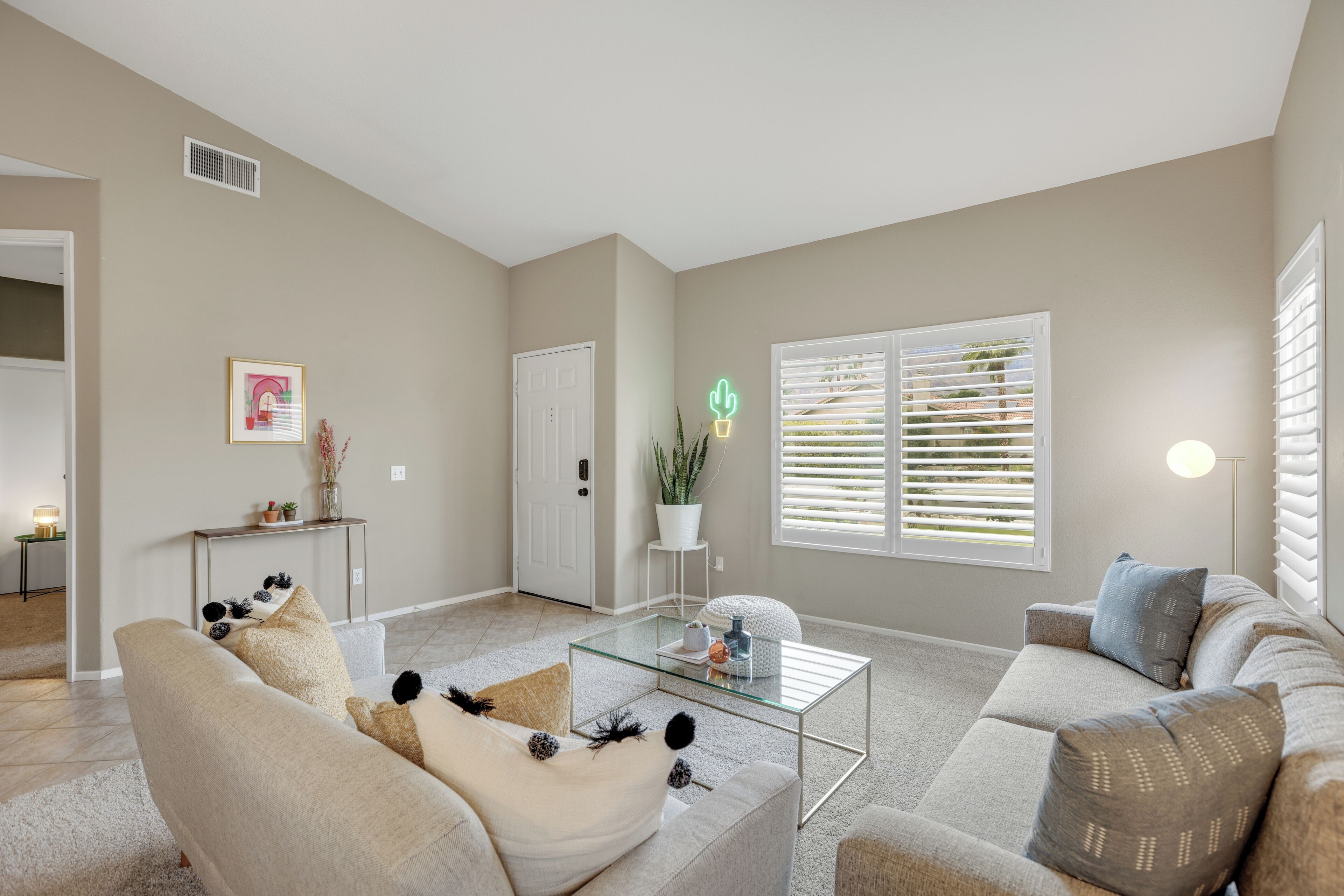 A spacious living room with a neutral color palette, a glass coffee table, and a comfortable seating area.
