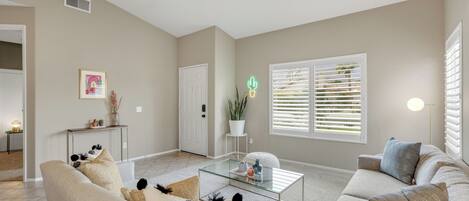 A spacious living room with a neutral color palette, a glass coffee table, and a comfortable seating area.