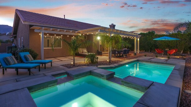 A swimming pool with a patio area, outdoor furniture, and string lights. - Shannon (Palm Springs)